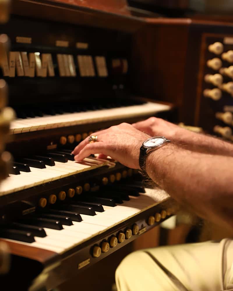 A musician's hands playing a traditional pipe organ during a service