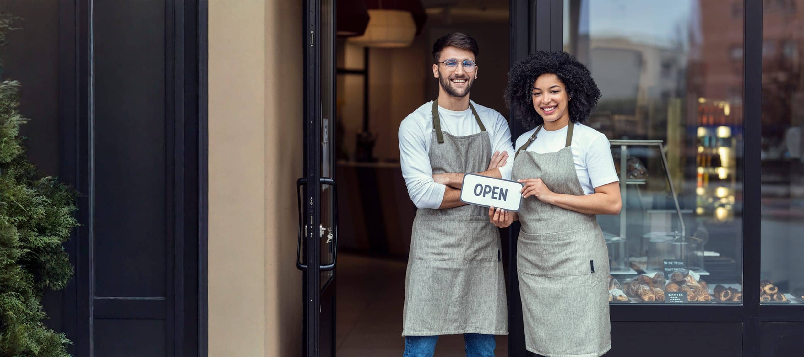 Small-business owners holding an OPEN sign outside their storefront