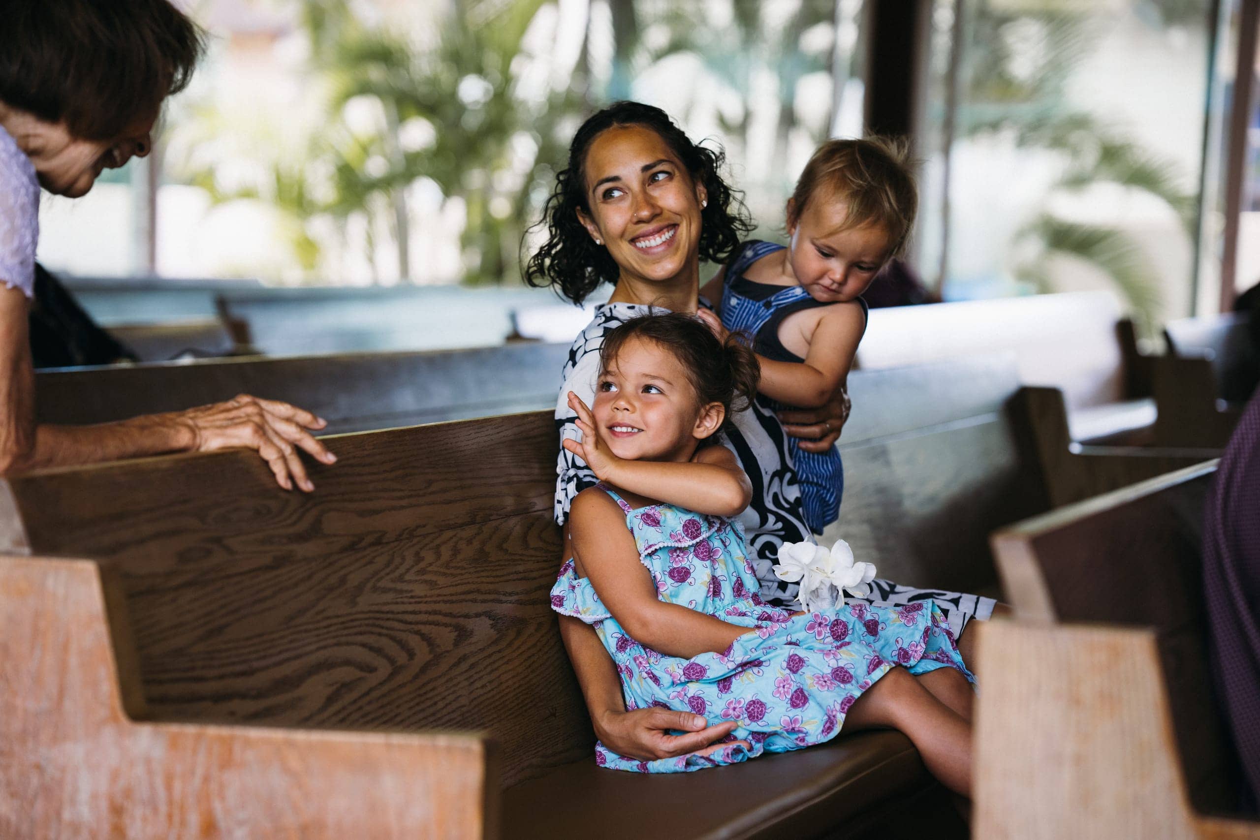 A smiling mother holding her two young children in a church pew