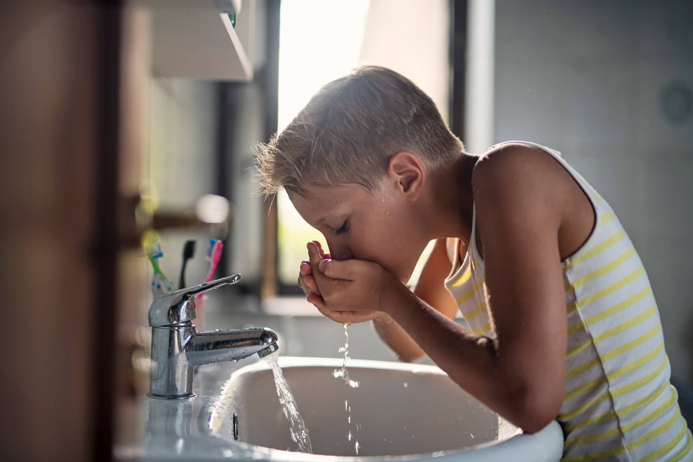 A child drinking clean tap water from cupped hands at a sink